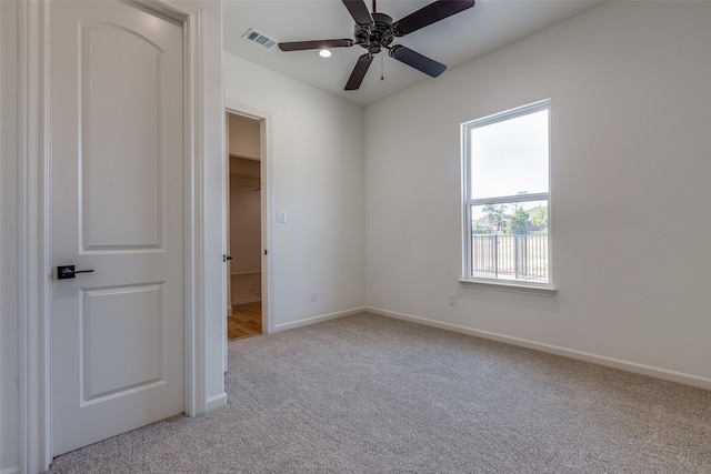 unfurnished bedroom with light carpet, a closet, ceiling fan, and a spacious closet