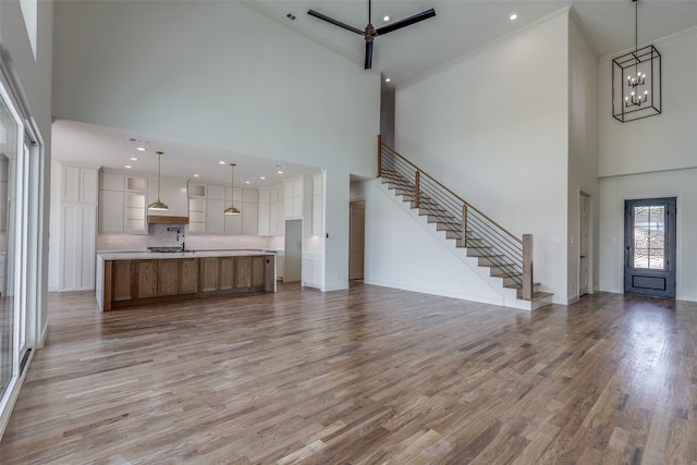 unfurnished living room with ornamental molding, an inviting chandelier, a towering ceiling, and light hardwood / wood-style floors