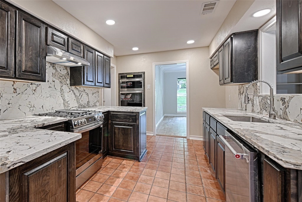 kitchen featuring light stone counters, light tile patterned flooring, dark brown cabinets, stainless steel appliances, and decorative backsplash