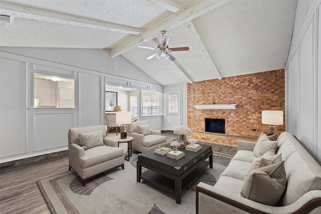 living room with hardwood / wood-style flooring, lofted ceiling with beams, a brick fireplace, a textured ceiling, and ceiling fan