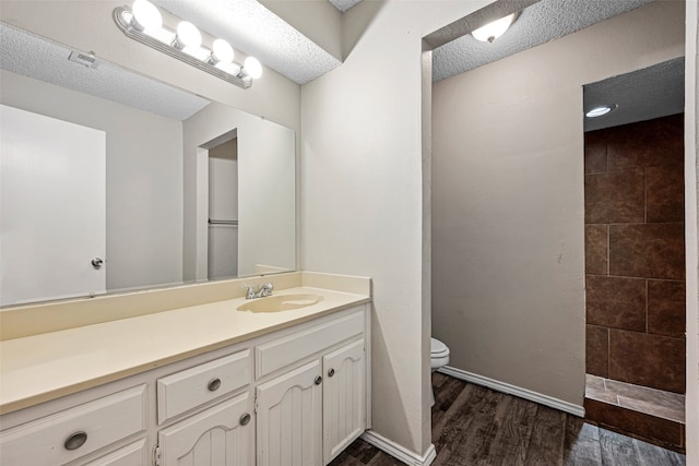 bathroom featuring tiled shower, toilet, wood-type flooring, vanity, and a textured ceiling