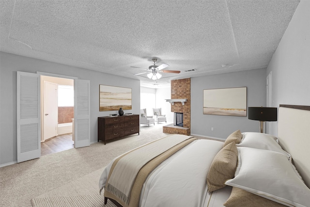 bedroom with a brick fireplace, a textured ceiling, ensuite bathroom, and ceiling fan