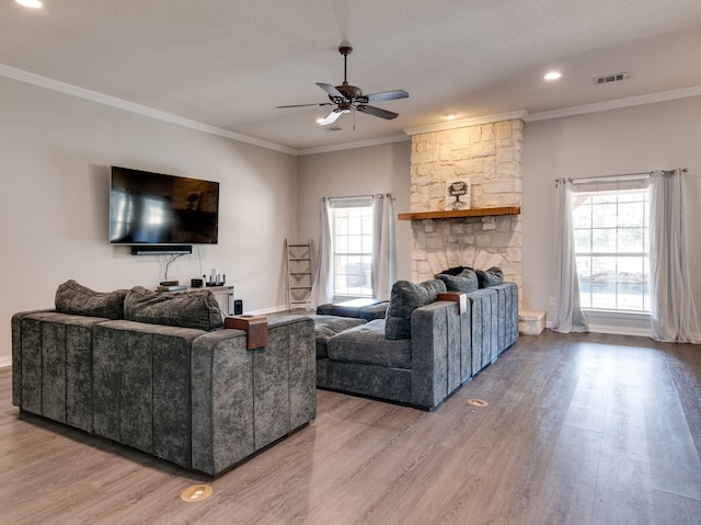 living room with crown molding, a stone fireplace, hardwood / wood-style floors, and ceiling fan