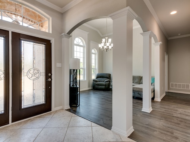 foyer featuring light wood-type flooring, ornamental molding, an inviting chandelier, and ornate columns