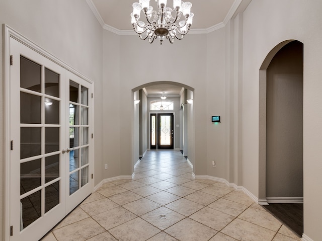 tiled entrance foyer with crown molding, a towering ceiling, a chandelier, and french doors