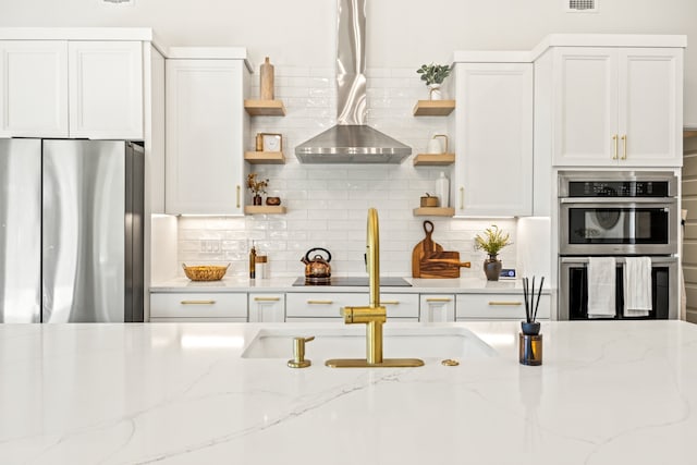 kitchen featuring stainless steel appliances, light stone counters, exhaust hood, and white cabinetry