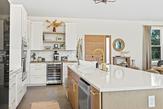 kitchen with a kitchen island with sink, tasteful backsplash, sink, white cabinetry, and wine cooler