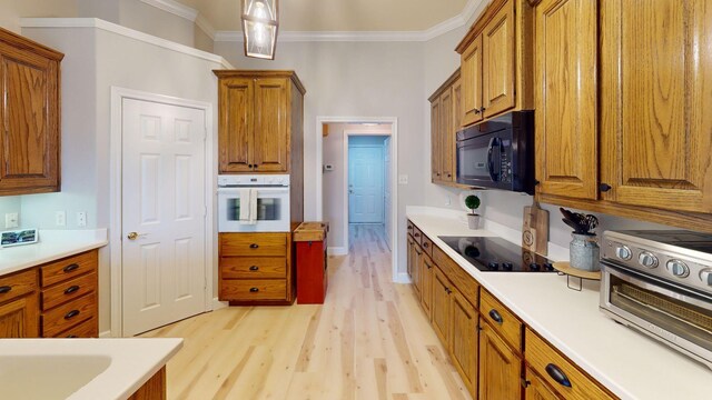 kitchen featuring decorative light fixtures, crown molding, light hardwood / wood-style floors, and black appliances