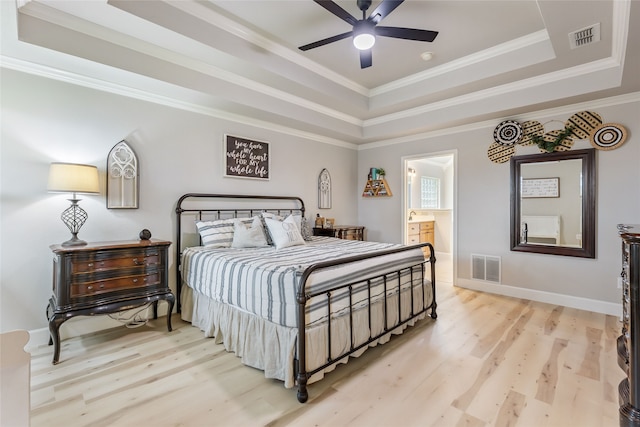 bedroom with a tray ceiling, light hardwood / wood-style flooring, ensuite bathroom, crown molding, and ceiling fan