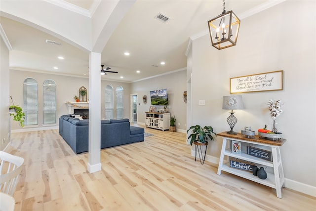 living room with ceiling fan with notable chandelier, ornamental molding, and light hardwood / wood-style flooring