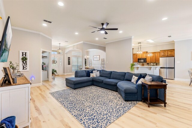 living room featuring light wood-type flooring, ceiling fan with notable chandelier, and crown molding