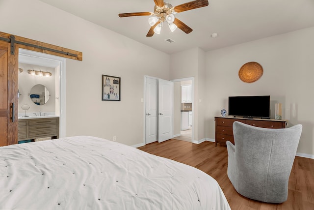 bedroom featuring light hardwood / wood-style flooring, a barn door, connected bathroom, and ceiling fan