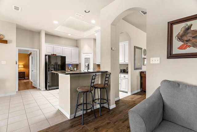 kitchen with a breakfast bar area, light hardwood / wood-style flooring, kitchen peninsula, black refrigerator with ice dispenser, and white cabinetry