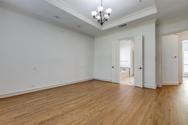 spare room featuring a chandelier, crown molding, a raised ceiling, and light wood-type flooring