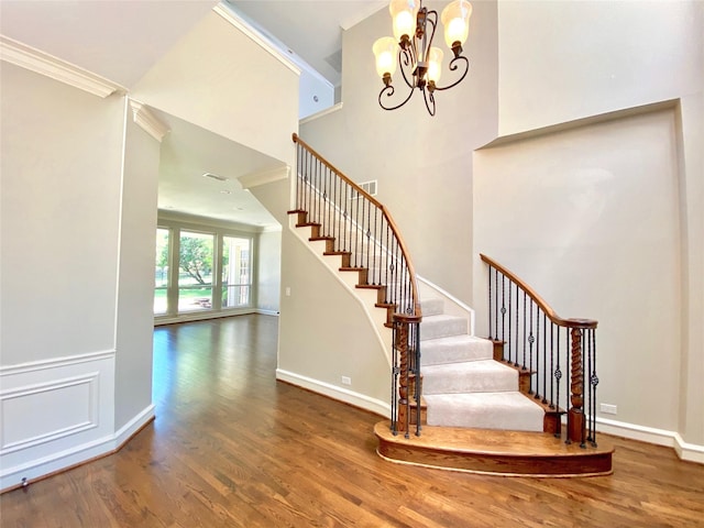 staircase featuring hardwood / wood-style flooring, ornamental molding, an inviting chandelier, and a high ceiling