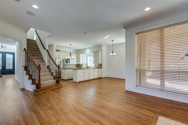 unfurnished living room featuring sink, an inviting chandelier, ornamental molding, french doors, and light wood-type flooring