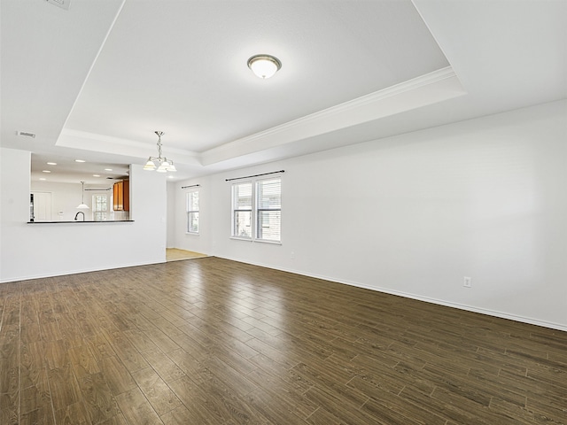 unfurnished living room with a tray ceiling, crown molding, dark hardwood / wood-style floors, and an inviting chandelier