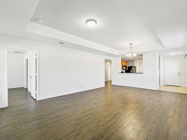 unfurnished living room with a raised ceiling, a chandelier, and dark wood-type flooring