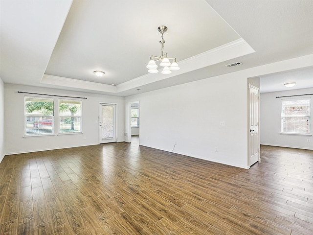 empty room featuring dark wood-type flooring, a tray ceiling, a chandelier, and crown molding