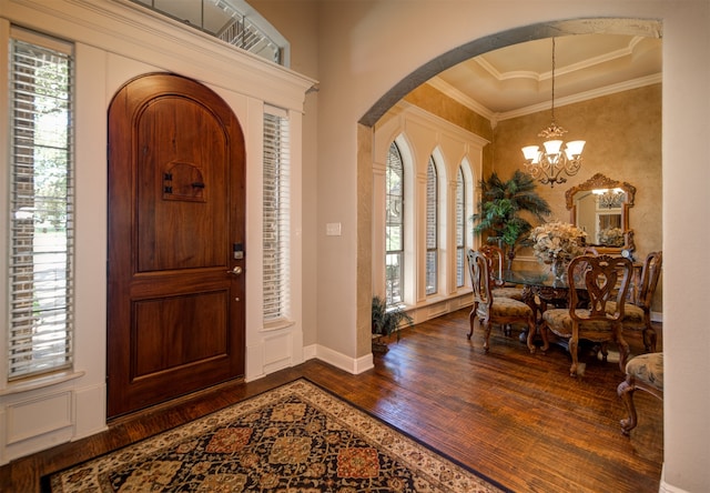 foyer with a notable chandelier, a raised ceiling, ornamental molding, and dark hardwood / wood-style flooring