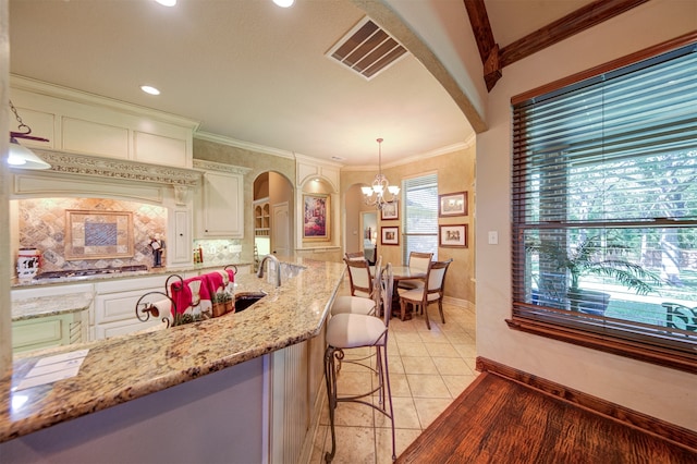 kitchen with pendant lighting, a breakfast bar, a notable chandelier, ornamental molding, and light stone countertops