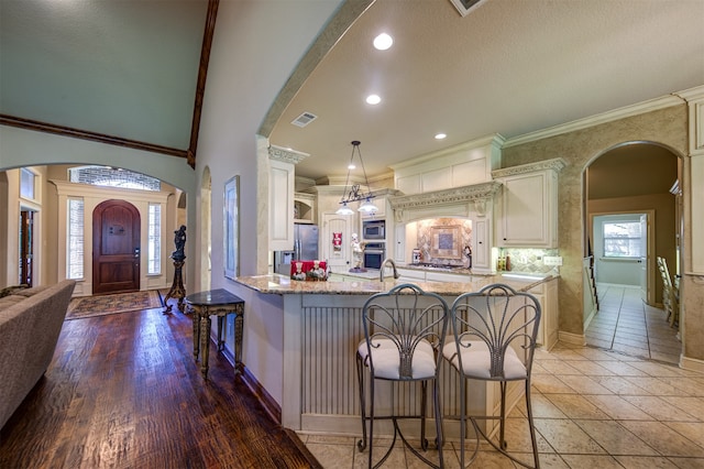 kitchen with ornamental molding, decorative light fixtures, appliances with stainless steel finishes, a breakfast bar area, and hardwood / wood-style floors