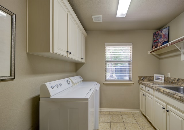 laundry area featuring washer and clothes dryer, cabinets, light tile patterned floors, and a textured ceiling