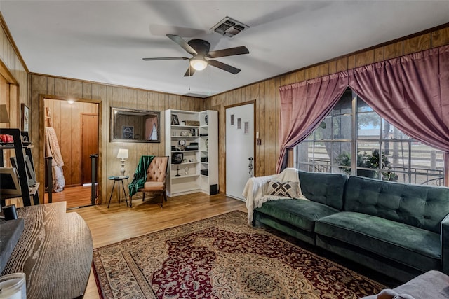 living room with wood-type flooring, ornamental molding, ceiling fan, and wood walls