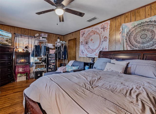 bedroom featuring hardwood / wood-style flooring, ceiling fan, ornamental molding, and wooden walls