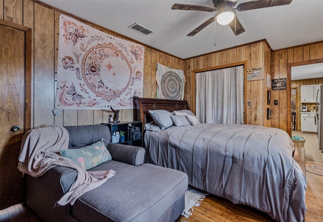 bedroom with ornamental molding, wooden walls, ceiling fan, and light hardwood / wood-style floors