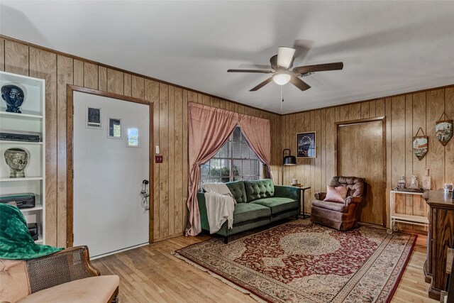 living room with ceiling fan, light hardwood / wood-style floors, and wood walls