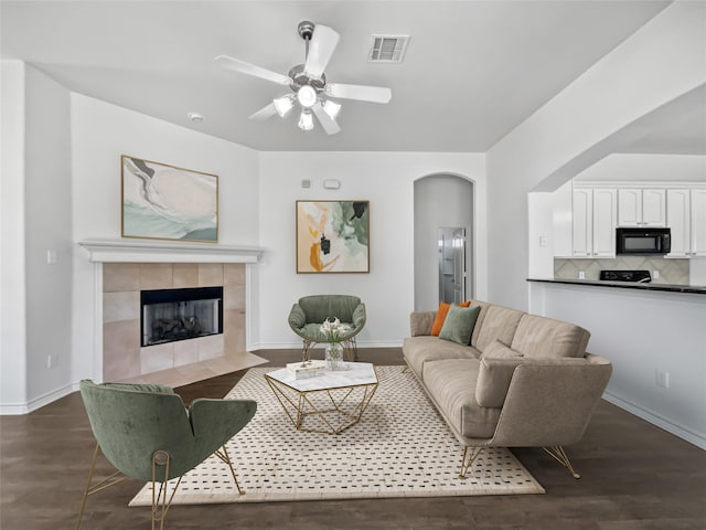 living room featuring a tiled fireplace, ceiling fan, and dark hardwood / wood-style flooring