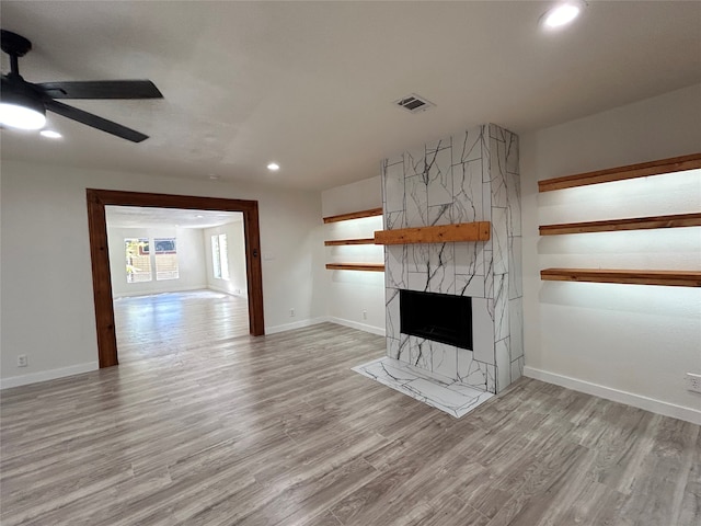 unfurnished living room with a large fireplace, light hardwood / wood-style flooring, and ceiling fan