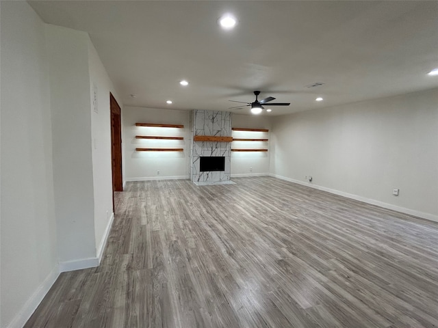 unfurnished living room featuring hardwood / wood-style flooring, ceiling fan, and a stone fireplace