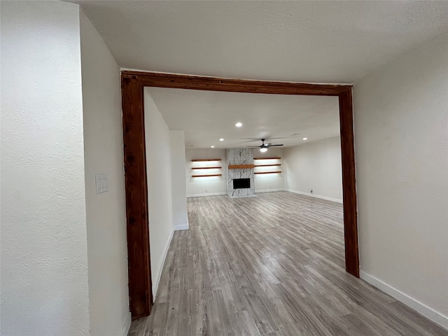 unfurnished living room featuring ceiling fan, light hardwood / wood-style floors, a textured ceiling, and a stone fireplace