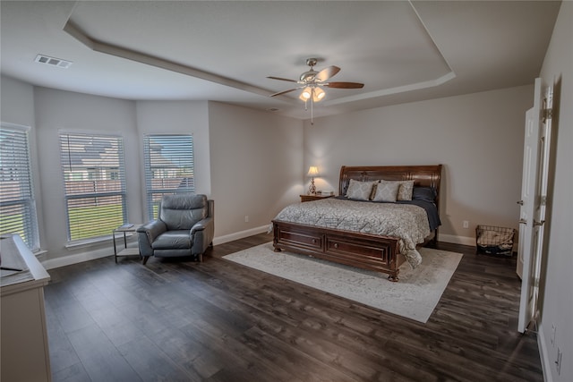 bedroom with a raised ceiling, dark wood-type flooring, and ceiling fan