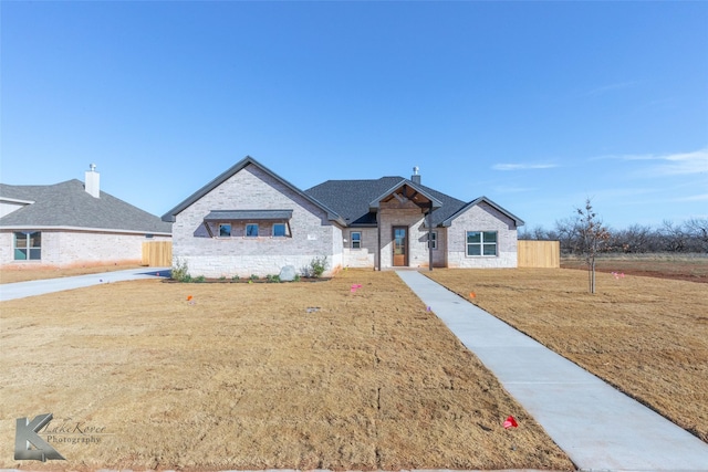 view of front of house with stone siding, a chimney, fence, and a front lawn