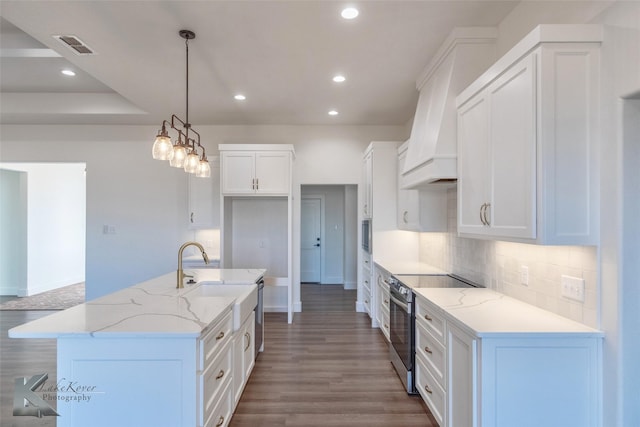 kitchen with electric range, light stone counters, decorative light fixtures, a kitchen island with sink, and white cabinetry