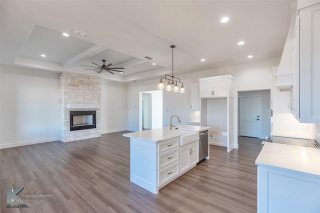 kitchen featuring hanging light fixtures, light stone countertops, a center island with sink, and white cabinets