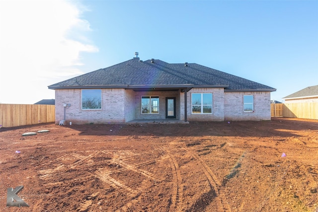 rear view of property with roof with shingles, fence, and brick siding