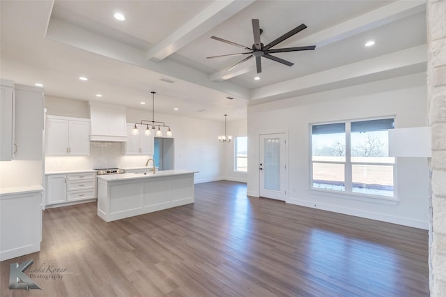 kitchen featuring light countertops, a center island with sink, decorative light fixtures, white cabinetry, and custom range hood