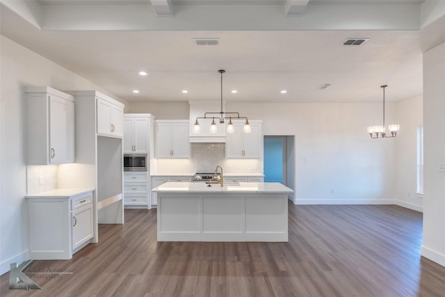 kitchen featuring visible vents, a kitchen island with sink, built in microwave, light countertops, and white cabinetry