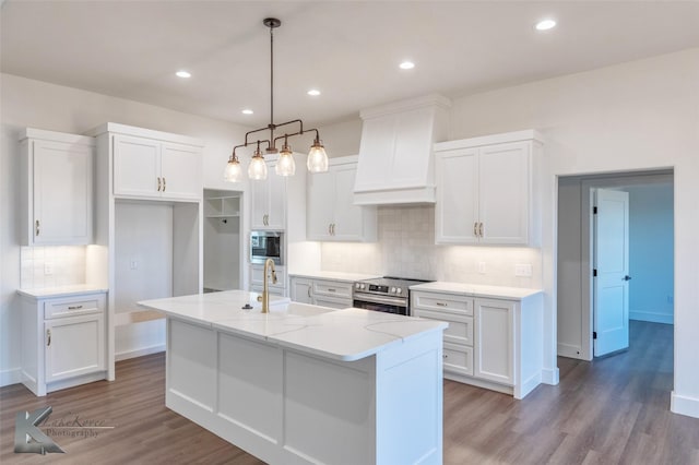 kitchen featuring an island with sink, wall chimney range hood, appliances with stainless steel finishes, and white cabinets