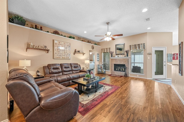 living room featuring a tiled fireplace, hardwood / wood-style floors, a textured ceiling, and ceiling fan