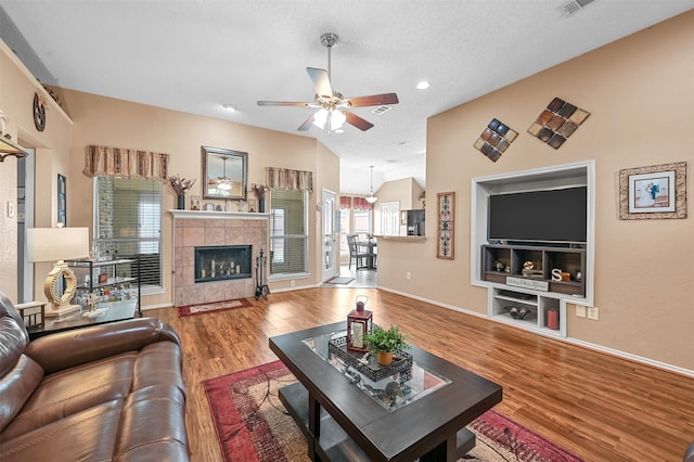 living room with ceiling fan, a tile fireplace, hardwood / wood-style flooring, and a textured ceiling