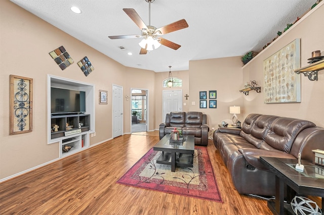 living room featuring a textured ceiling, wood-type flooring, built in shelves, and ceiling fan