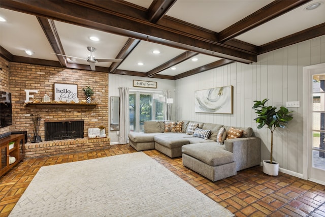 living room with ceiling fan, a fireplace, beamed ceiling, and crown molding