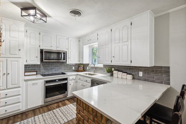 kitchen with kitchen peninsula, appliances with stainless steel finishes, dark hardwood / wood-style flooring, sink, and white cabinetry