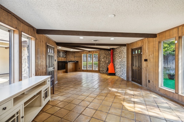 interior space with beamed ceiling, a textured ceiling, and wooden walls