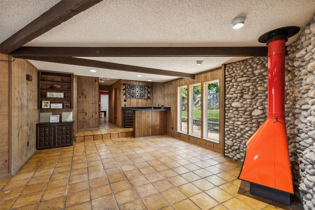 interior space featuring beamed ceiling, a textured ceiling, and wooden walls